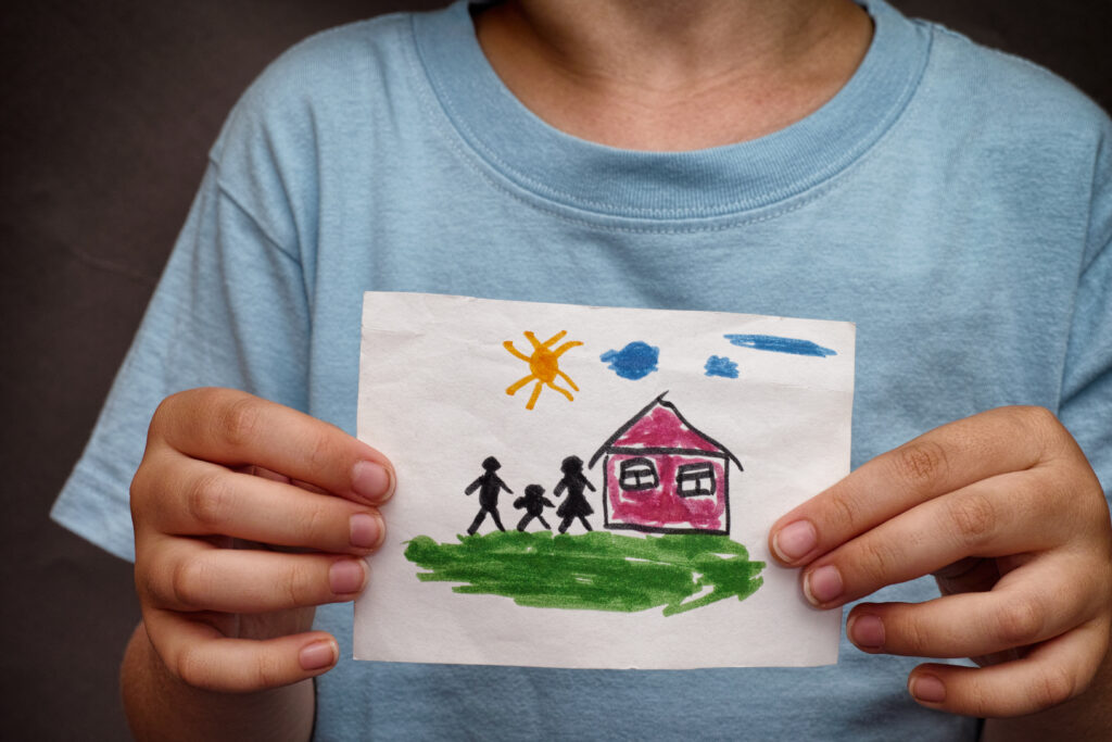 An image of a child holding a drawing of a house with family. Close up.