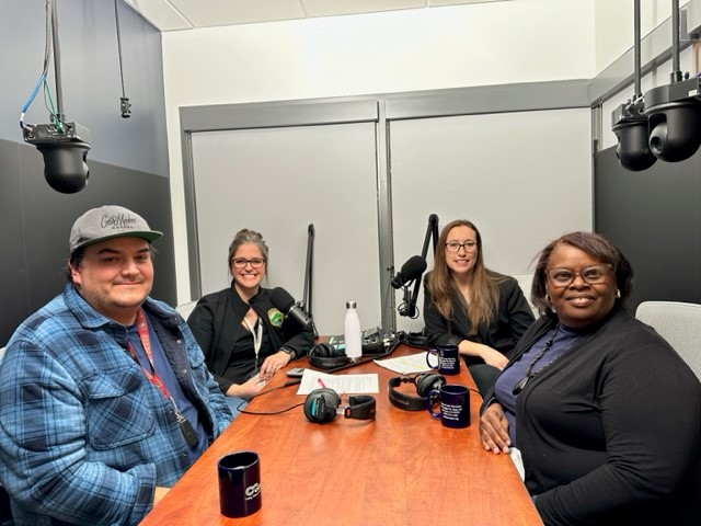 A photo of Juan De Dios Batiz, Head Start Policy Council parent; Kristi Jourdan, host & Director of Communications, Contra Costa County; Sarah Reich, CSB Interim Deputy Director; and Ruth Hunter, George Miller III Site Supervisor. All are seated at a wooden table, with mics in front of them. 