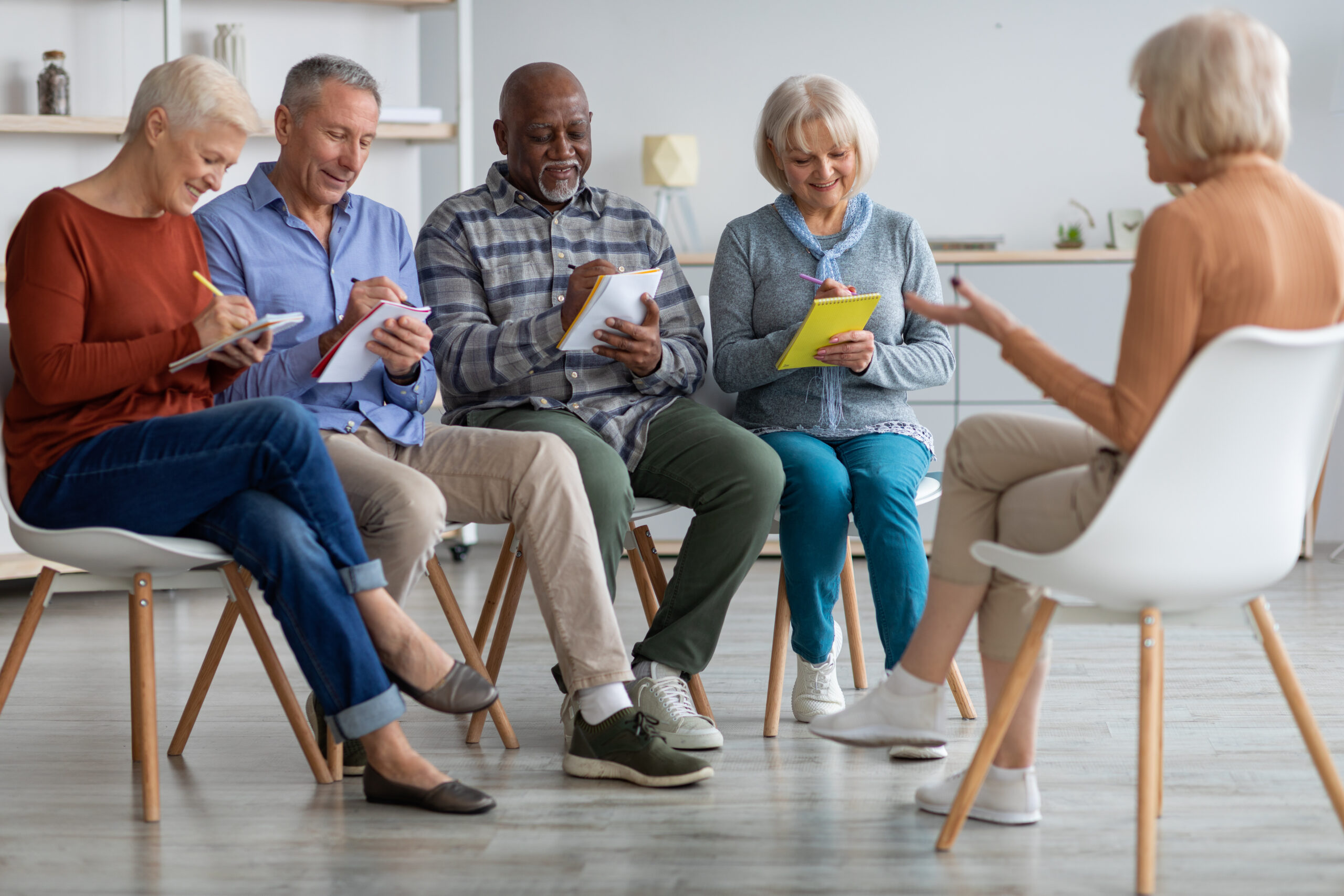 Multiracial group of cheerful elderly men and women sitting down in a class setting. 