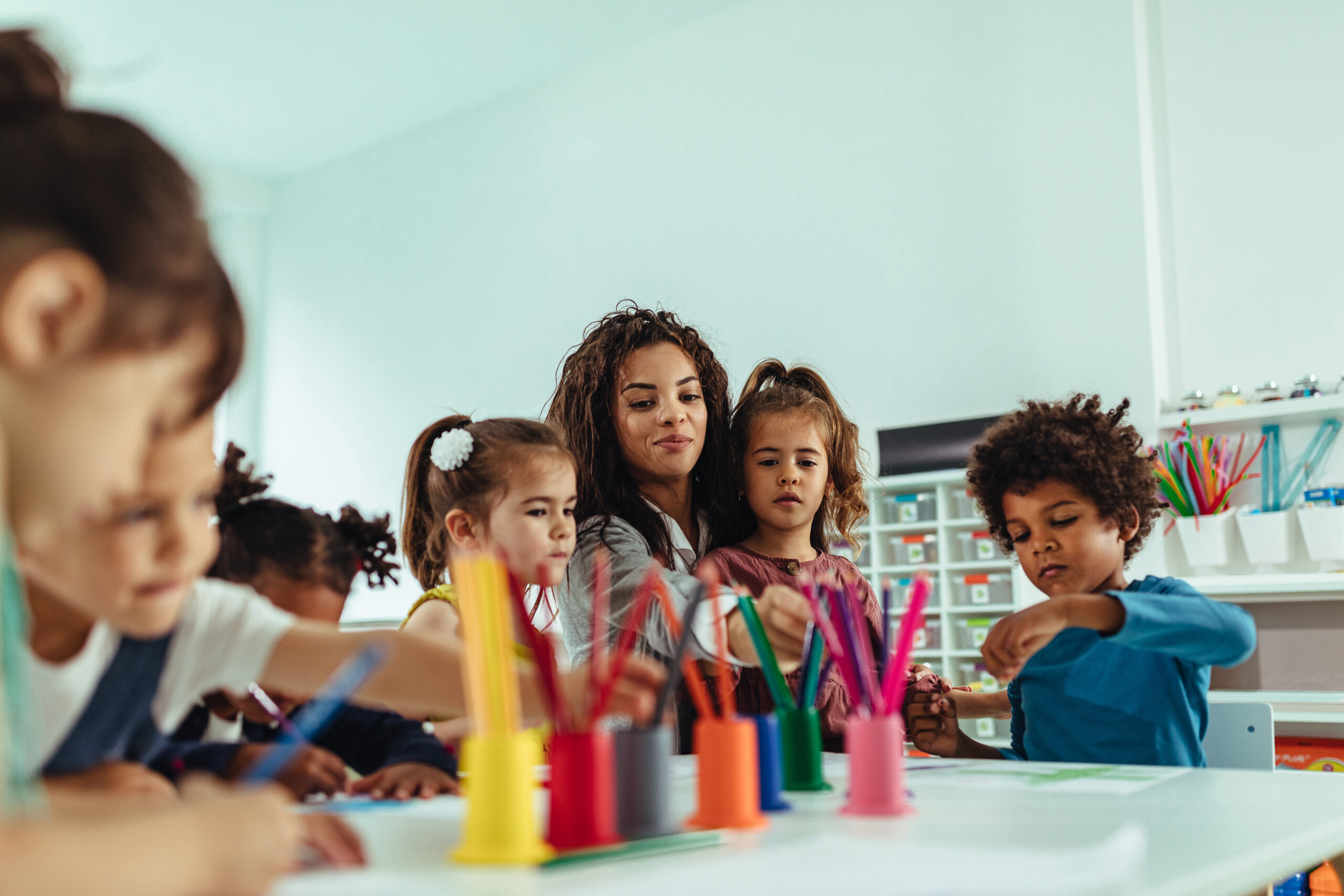 A group of preschoolers play arts and crafts with their teacher