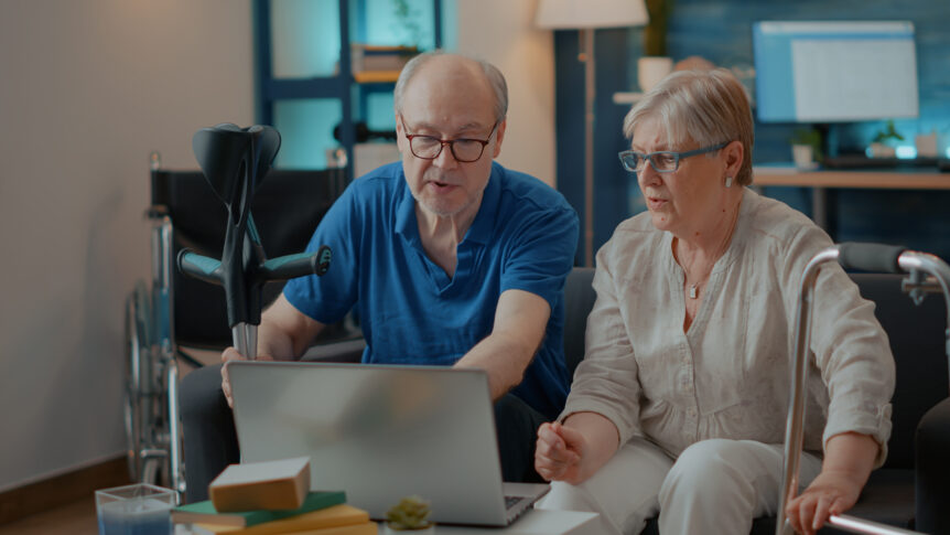 Two older adults look at a laptop together